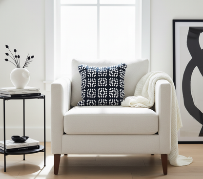 White armchair with a black and white crochet cushion and a white blanket in a bright living room.