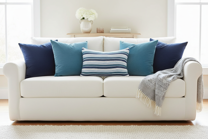 White sofa with blue cushions and a blue and white striped crochet cushions in a bright room