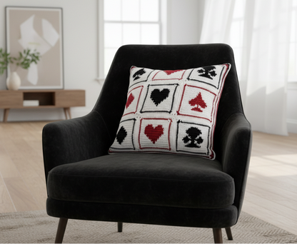 Black armchair with a decorative crochet cushion featuring hearts, clubs, diamonds, and spades in a living room setting.