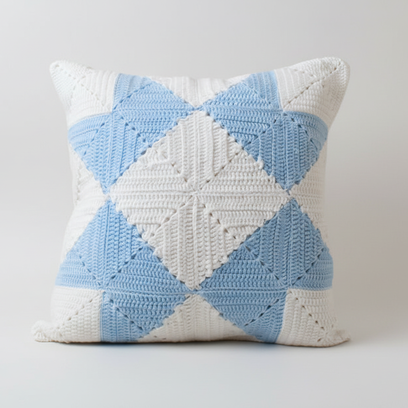 Crocheted pillow with blue and white diamond pattern on a light grey background