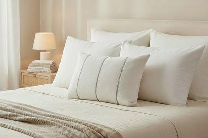 Neatly made bed with white pillows and an ivory linen cushions with grey leaf embroidery