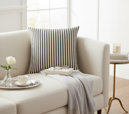 Cream sofa with striped ticking black and cream cushion grey throw blanket in a bright living room.ream