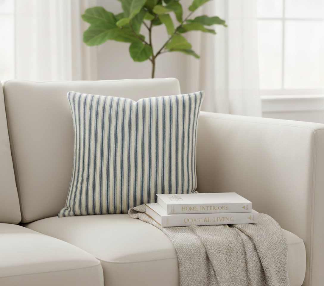 Cream sofa with a striped blue and cream ticking cushion and books on a blanket, with a plant in the background.