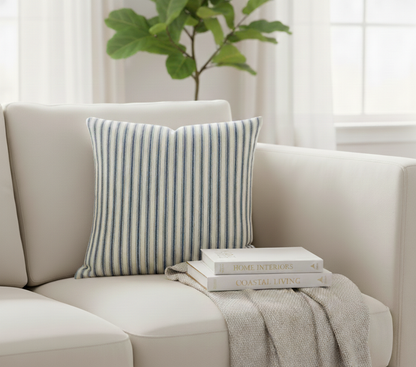 Cream sofa with a striped blue and cream ticking cushion and books on a blanket, with a plant in the background.